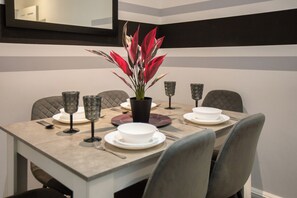 Une table à manger dressée avec des assiettes, des verres et des couverts, et une plante en pot placée au centre.