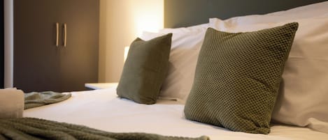 A neatly made bed with two pillows and a blanket, a dark-colored wardrobe, and a white wall.