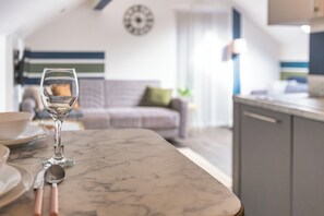 Ein Esstisch mit einem Weinglas und Besteck, ein Sofa und im Hintergrund eine Küchenzeile.