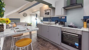 A modern kitchen with a built-in microwave, oven, and a coffee maker. There is a dining area with a table and bar stools. - South Pier Apartment 7 (Blackpool)