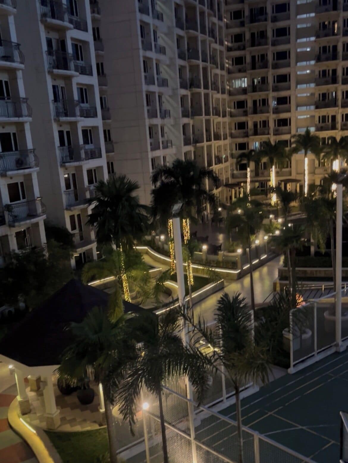 A multi-story hotel with balconies, palm trees, and a well-lit outdoor area.