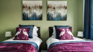 Een tweepersoonsbed met bijpassende hoofdeinden, twee nachtkastjes en twee aan de muur hangende schilderijen.