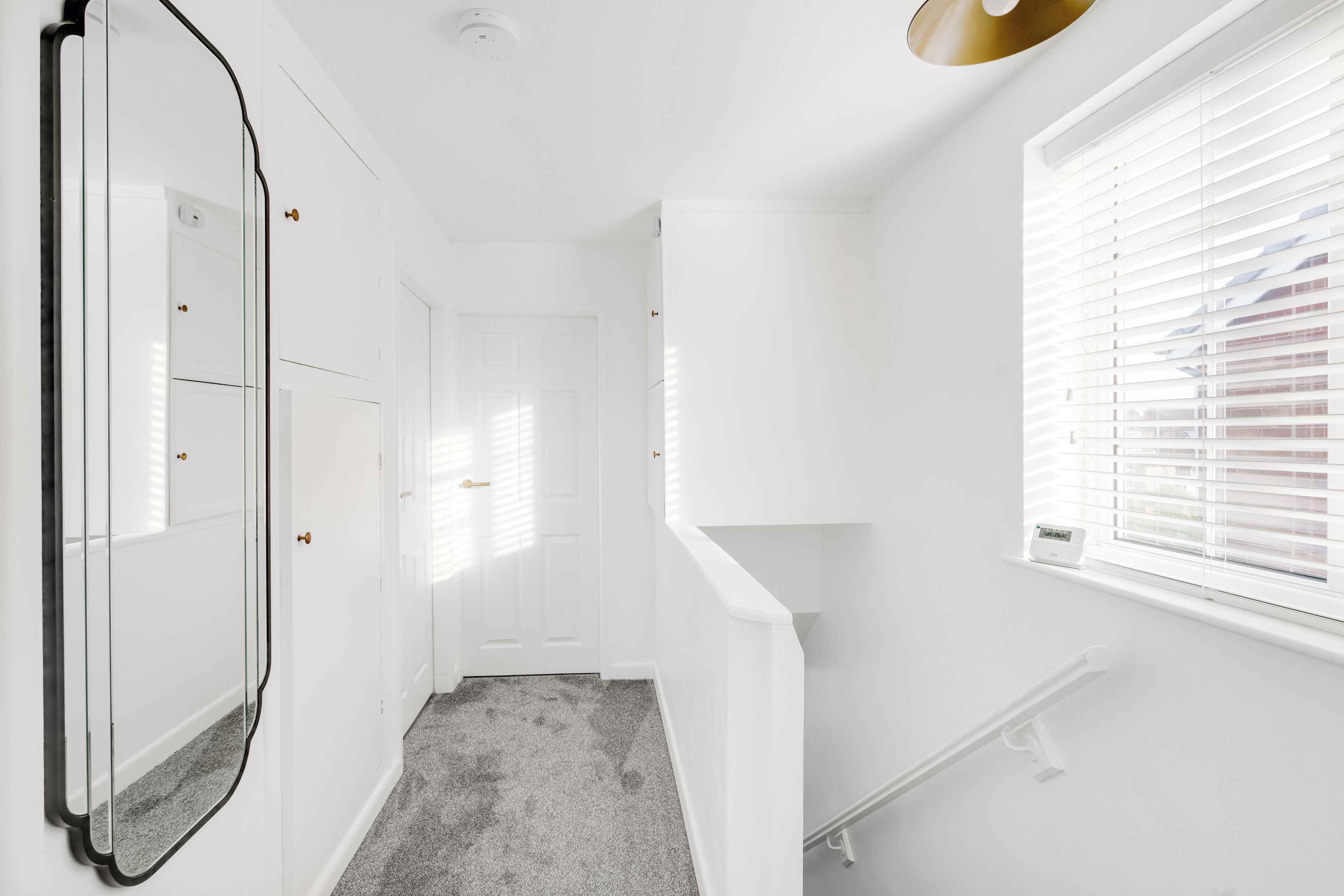 A hallway with a white door, a mirror, and a window with blinds.