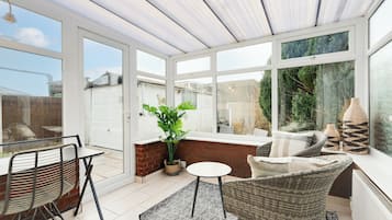 A conservatory with a glass door, a dining table, chairs, a small rug, and a wicker sofa.