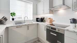 Een moderne keuken met witte kastjes, een inbouwoven en een raam met zonwering.