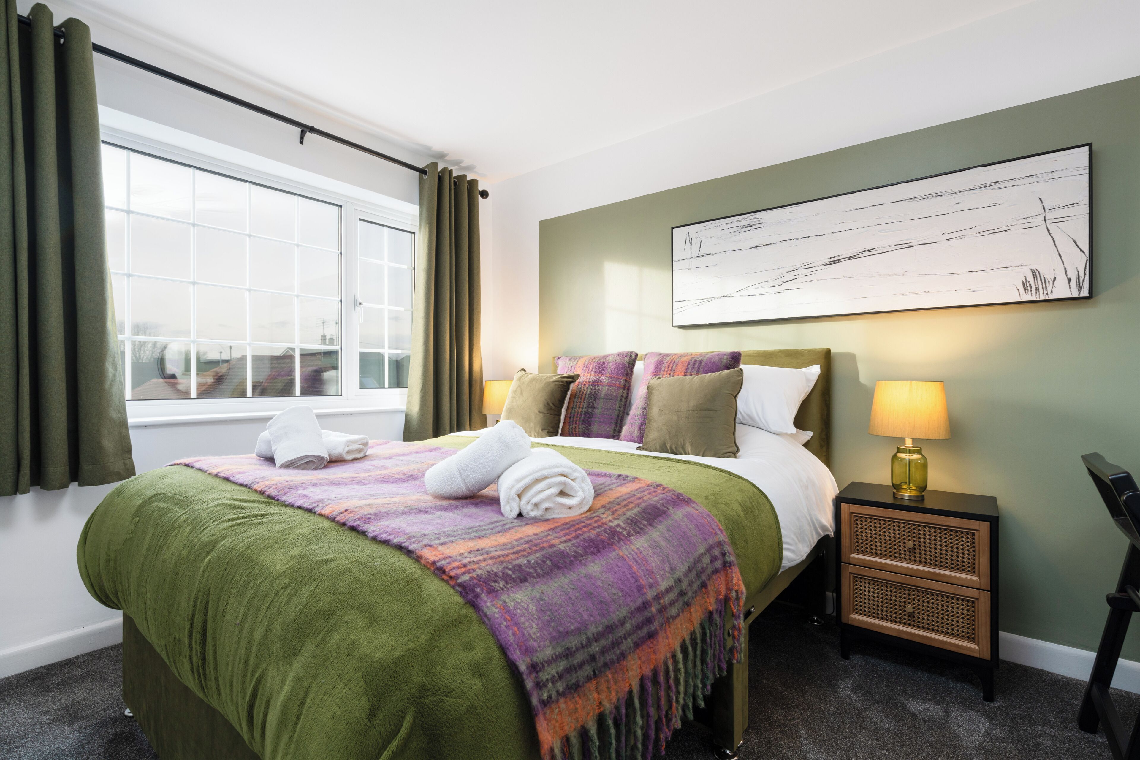 A hotel room with a bed, a nightstand, a lamp, and a window with curtains.