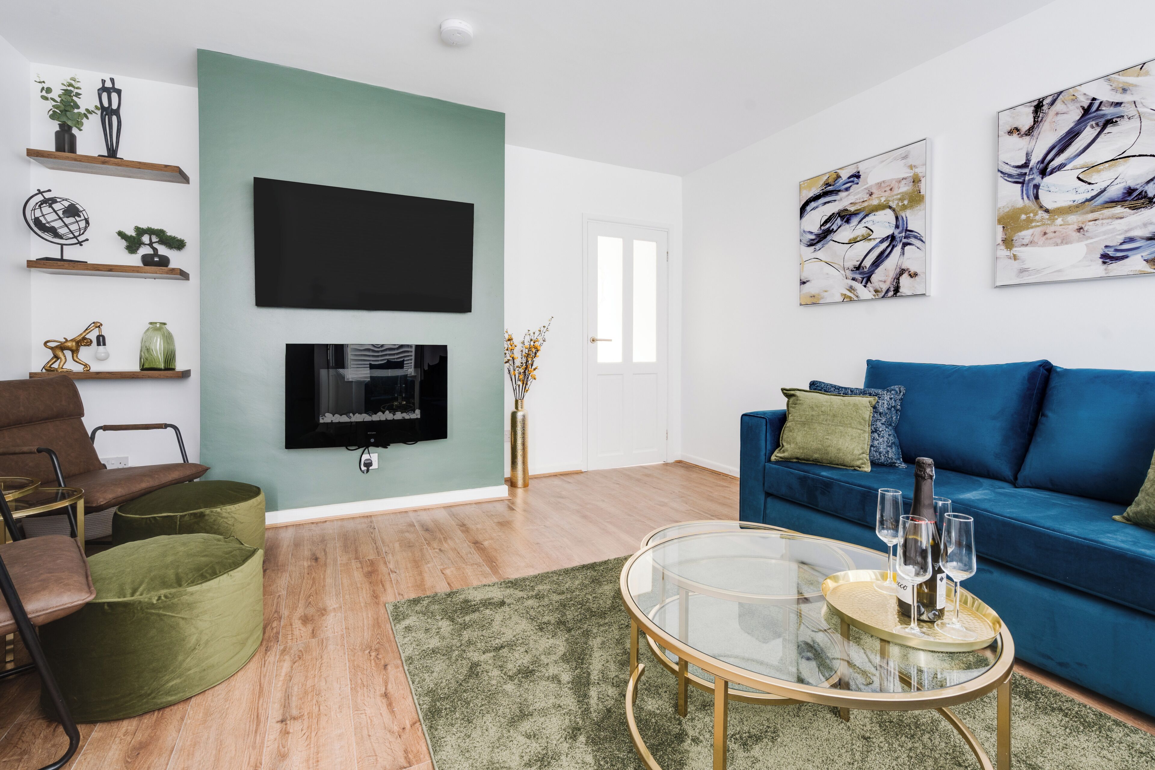 A modern living room with a flat-screen TV, a blue sofa, a green armchair, and a coffee table.