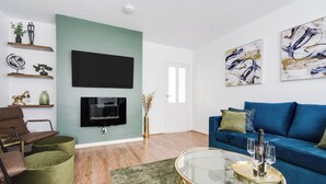 Een moderne woonkamer met een flatscreen televisie, een blauwe bank, een groene fauteuil en een salontafel.