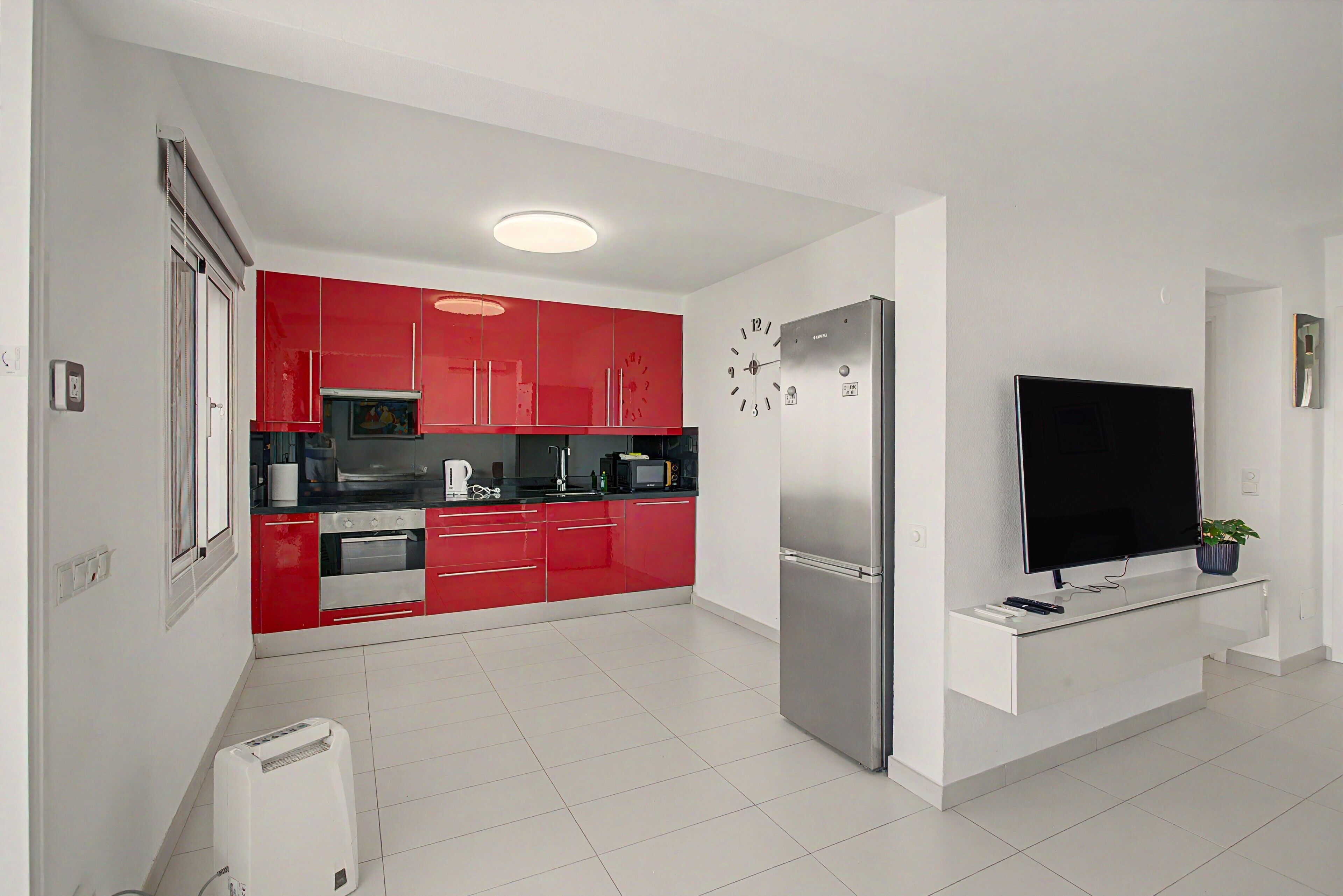 Une cuisine moderne avec des meubles de couleur rouge, un réfrigérateur en acier inoxydable et un téléviseur à écran plat fixé au mur.
