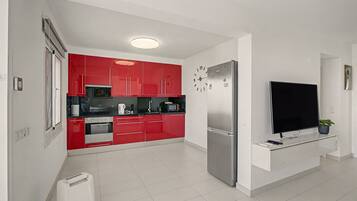 Une cuisine moderne avec des meubles de couleur rouge, un réfrigérateur en acier inoxydable et un téléviseur à écran plat fixé au mur.