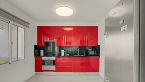 A compact kitchen with red cabinets, a built-in oven, and a microwave. - Nueva Suecia 805 – Beachfront Apartment with Terrace and Sea Views (San Bartolomé de Tirajana)