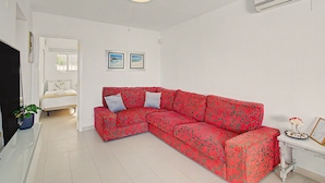 A modern living room with a red patterned sofa, a flat-screen TV, and a small table with decorative items. - Nueva Suecia 805 – Beachfront Apartment with Terrace and Sea Views (San Bartolomé de Tirajana)