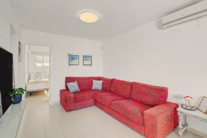 Uma sala de estar moderna com um sofá vermelho estampado, uma televisão de tela plana e uma mesinha com objetos decorativos.