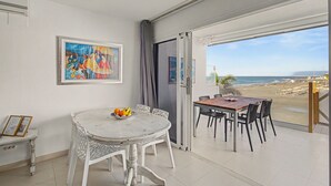 A room with a dining table and chairs, a painting on the wall, and a view of the beach through an open door. - Nueva Suecia 805 – Beachfront Apartment with Terrace and Sea Views (San Bartolomé de Tirajana)