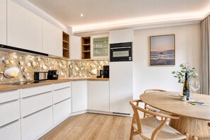 Une cuisine moderne avec des meubles blancs, un four encastré et un plan de travail agrémenté d’un pare-feu en forme de coquillage.