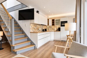 Eine moderne Küche mit integrierter Kochinsel, einer Holztreppe und einem flachbildfernseher, der über der Insel angebracht ist.