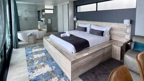 A modern bedroom with a large bed, a bathroom, and a seating area. - Ntomb'lele Ocean View Luxury Villas (Tugela Mouth)