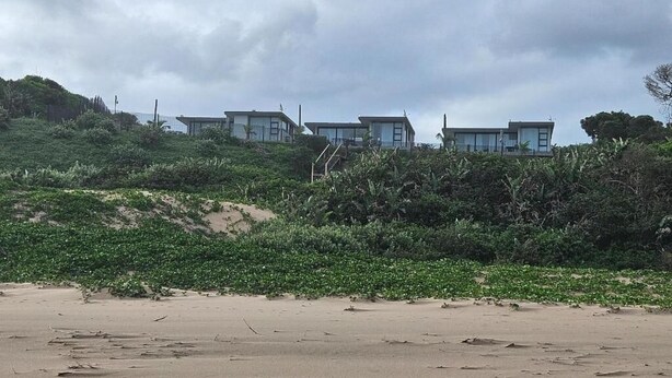 A beach with a row of modern beach houses, sandy terrain, and dense vegetation. - Ntomb'lele Ocean View Luxury Villas (Tugela Mouth)