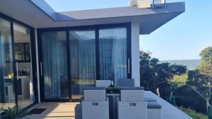 A modern house with a patio area featuring outdoor furniture and a glass door leading to an interior space. - Ntomb'lele Ocean View Luxury Villas (Tugela Mouth)