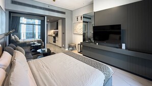 A modern hotel room with a large bed, a seating area with a sofa and chairs, a dining table, a kitchen area, and a TV mounted on the wall. - Canal View Studio Near Dubai Mall (Dubai)