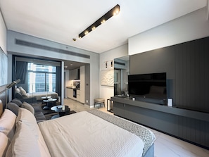 A modern hotel room with a large bed, a seating area with a sofa and chairs, a dining table, a kitchen area, and a TV mounted on the wall. - Canal View Studio Near Dubai Mall (Dubai)