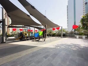 An outdoor play area with a slide, swings, and a shaded seating area. - Canal View Studio Near Dubai Mall (Dubai)