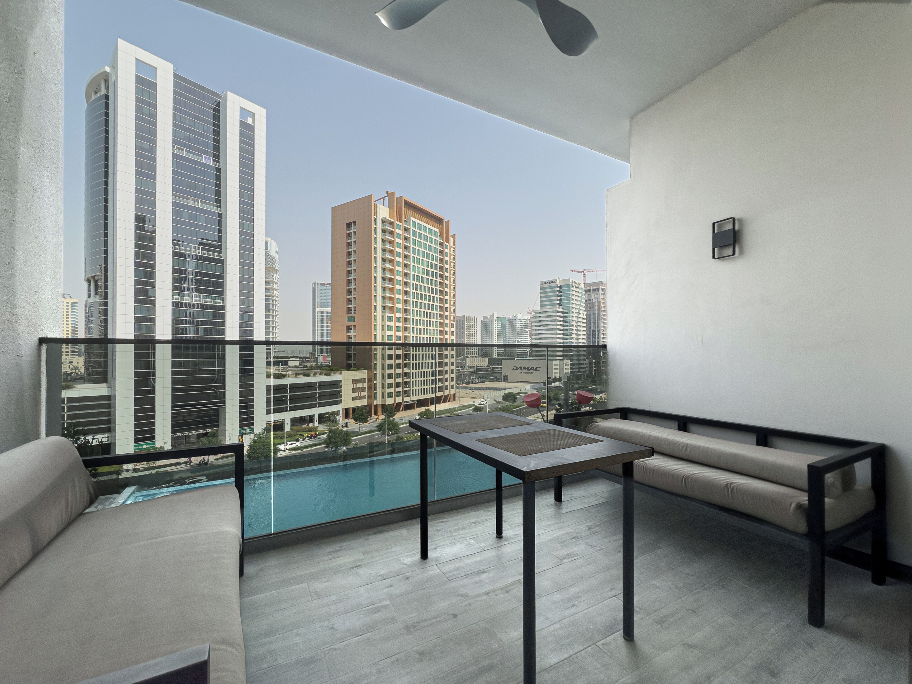 Een balkon met uitzicht op hoge gebouwen, een zwembad en een zitgedeelte met een tafel.