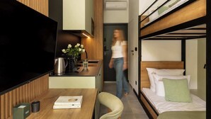 Ein Zimmer mit Etagenbett, Schreibtisch, Flachbildfernseher, Kaffeemaschine und Blumen in einer Vase.