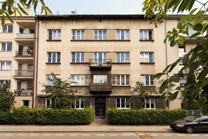 Ein mehrgeschossiges Wohngebäude mit Balkonen, einem verschlossenen Eingangsbereich und einem Parkplatz.