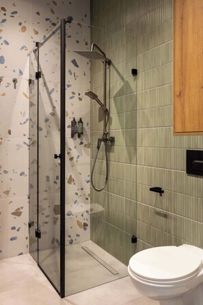 Ein modernes Badezimmer mit Duschkabine aus Glas, Toilette und einer Wand in Grün gefliest.