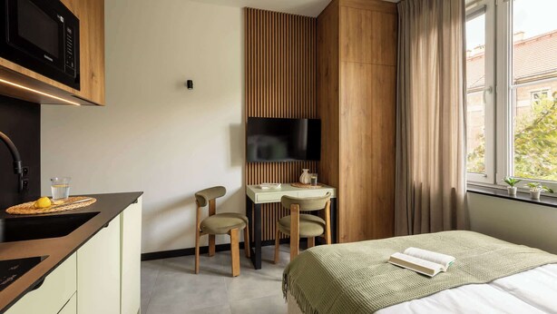 A hotel room with a kitchenette, a desk with a chair, a bed, and a TV mounted on the wall. - Pułaskiego 7C | Perfect for Couples | AC (Kraków)