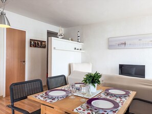 Ein Essbereich mit einem Holztisch, gedeckt für vier Personen, Stühlen, einer Couch, einem Fernseher und einer Wand mit einem Gemälde.