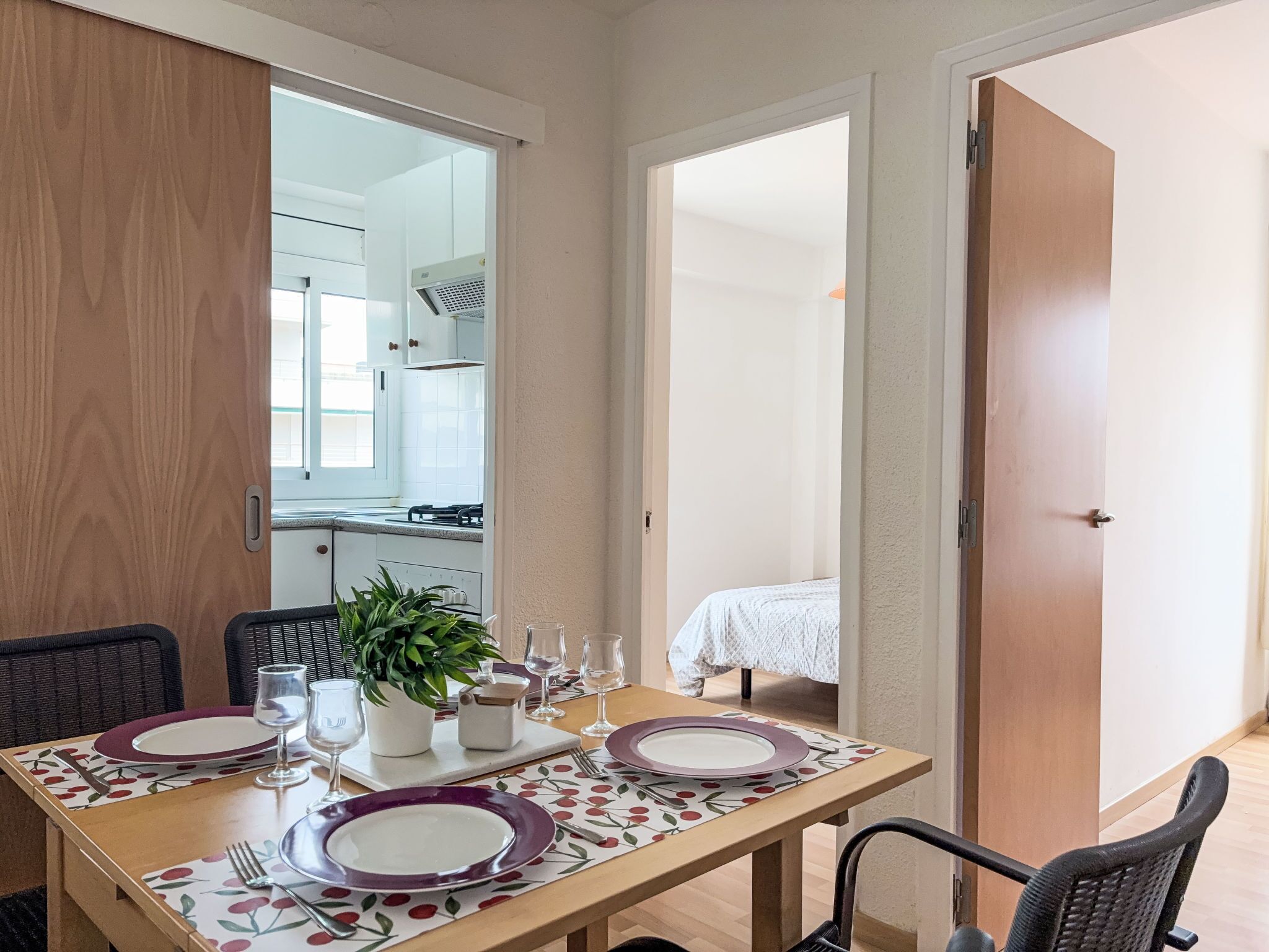 A dining area with a table set for four, chairs, a potted plant, and a view into the kitchen.