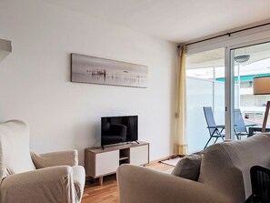 Ein modernes Wohnzimmer mit einem Flachbildfernseher auf einem Holzbalken, einem großen Fenster mit Blick auf einen Balkon und einem abstrakten Kunstwerk an der Wand.