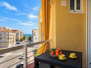 Ein Balkon mit Tisch, gelben Vorhängen und Blick auf das Meer und Gebäude.