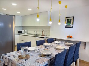 A modern kitchen with white cabinets, a microwave, and a coffee maker. There is a dining table set with plates, glasses, and a centerpiece. - Apartment Clara by Interhome (St Antoni de Calonge)