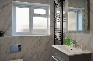 A bathroom with a marble floor, a white sink with a mirror above it, and a window with frosted glass. - Freshly Refurbished 2BDR Flat in Catford Bridge (Greater London)