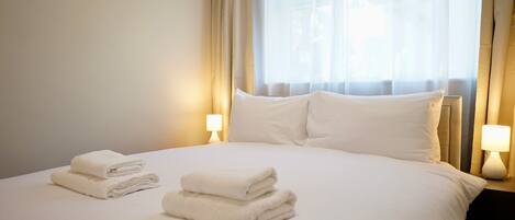 A hotel room with a neatly made bed, two bedside lamps, and a window with curtains.