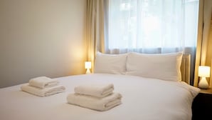 A hotel room with a neatly made bed, two bedside lamps, and a window with curtains. - Freshly Refurbished 2BD Flat in Catford Bridge (Greater London)