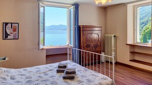 A bedroom with a bed, a view of the sea, a radiator, and a wooden cabinet. - Casa Yakamos by Interhome (Brissago)
