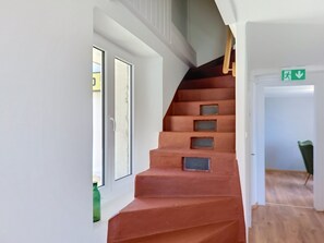 A staircase with a wooden handrail and a green emergency exit sign. - Casa Yakamos by Interhome (Brissago)