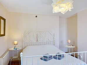 A white metal bed with a decorative headboard, two bedside tables with lamps, and a ceiling light fixture. - Casa Yakamos by Interhome (Brissago)