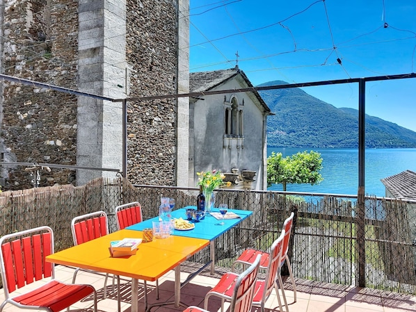 An outdoor dining area with a table and chairs, overlooking a lake and a mountain. - Casa Yakamos by Interhome (Brissago)