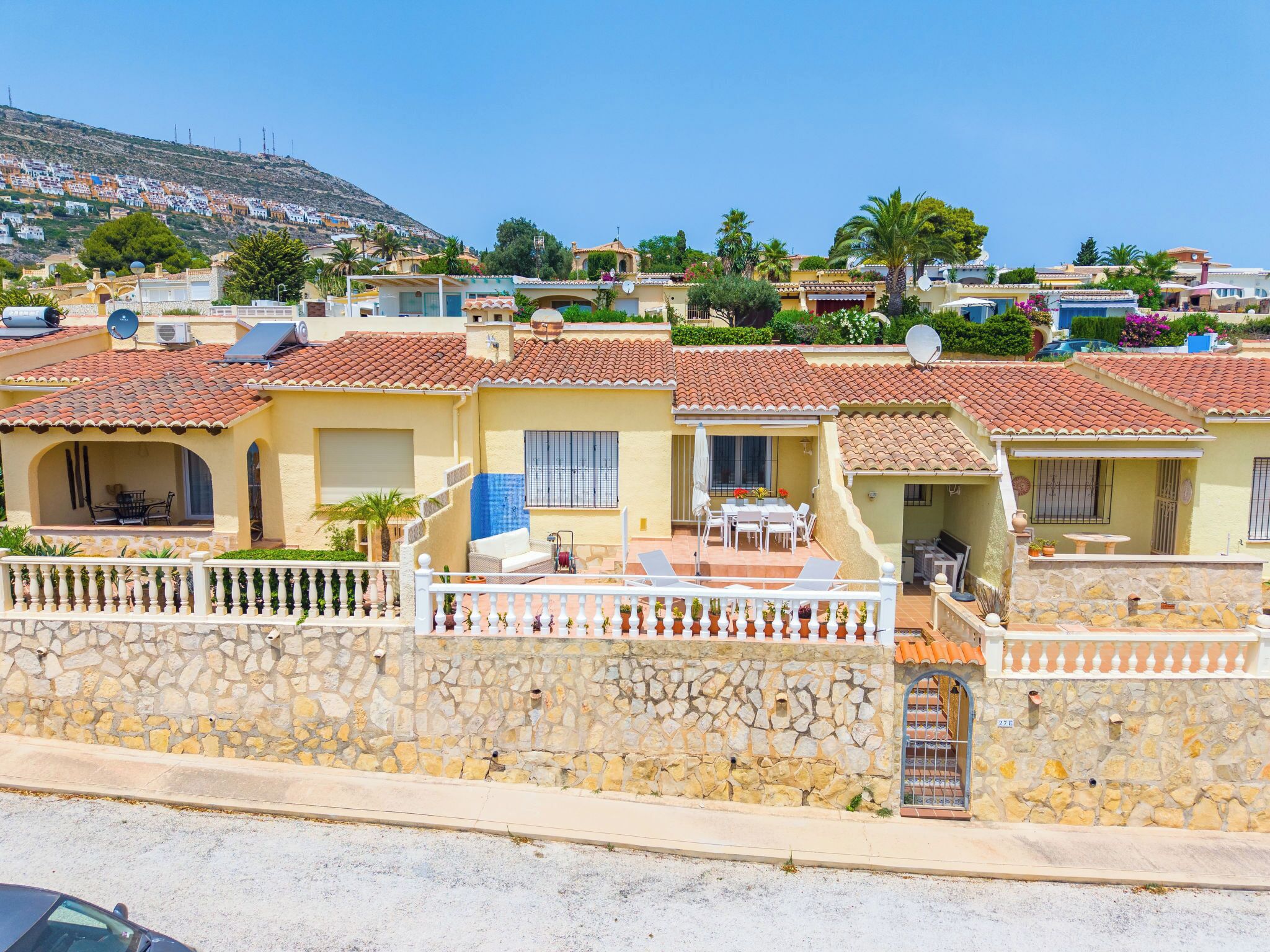 A coastal residential area with terracotta-tiled buildings, stone walls, and a clear view of the sea.