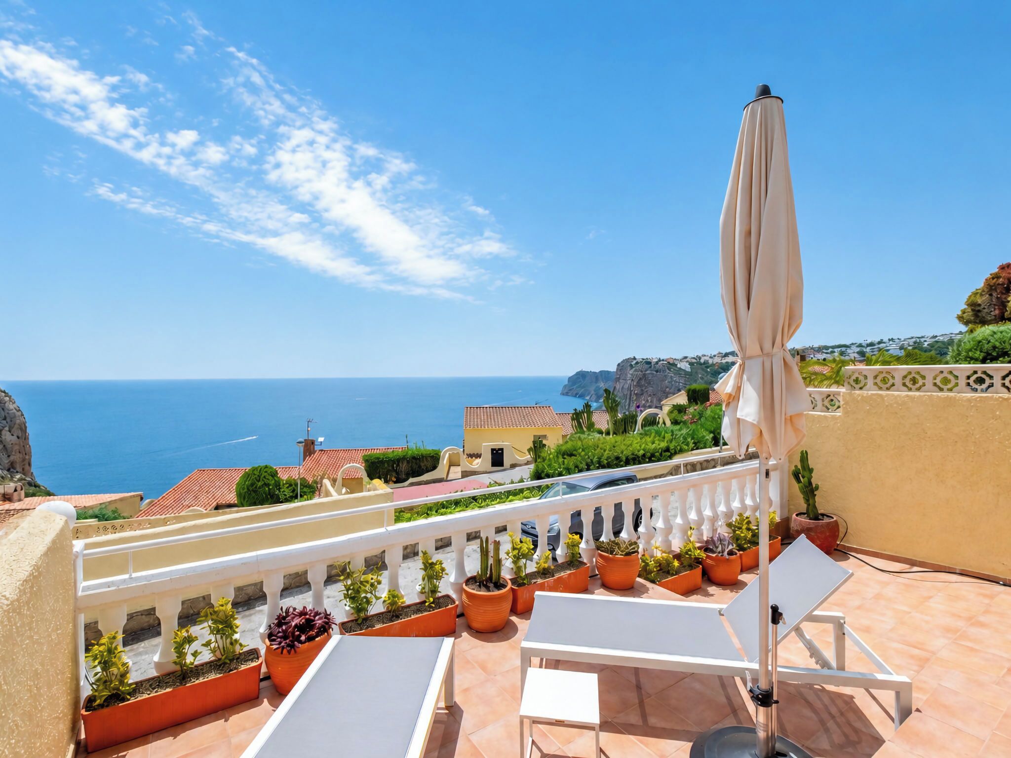 A terrace with a view of the sea, outdoor furniture, and potted plants.