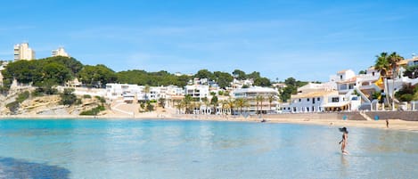 Un pueblo costero con edificios a lo largo de la playa, agua azul cristalina y una persona de pie en el agua.