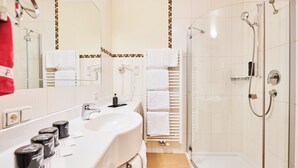 Ett modernt badrum med en duschavdelning med glasväggar, en vit tvättställ och en spegel med handdukshängare.