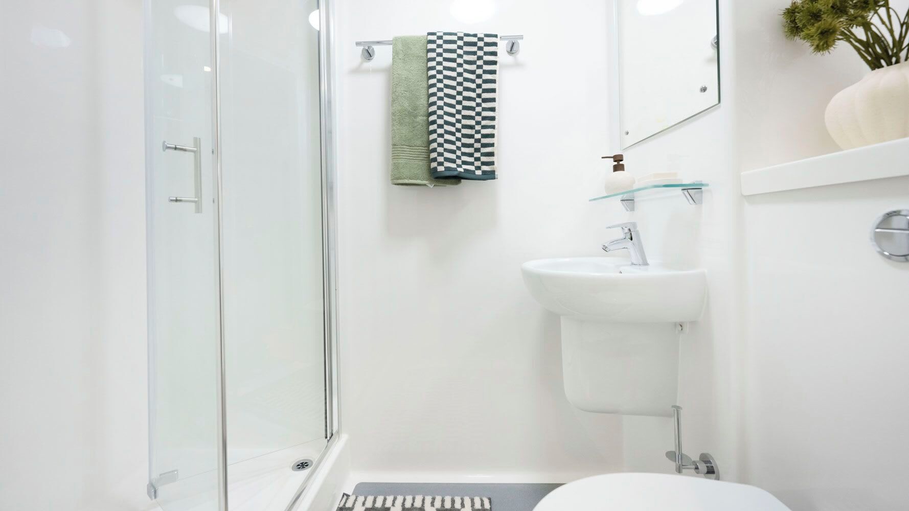 Une salle de bain moderne avec une douche à parois de verre, un lavabo blanc et une serviette à carreaux.