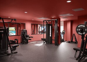 Ein Fitnessraum mit unterschiedlichen Trainingsgeräten, darunter ein Squat-Rack, eine Gewichtbank und Kurzhanteln.