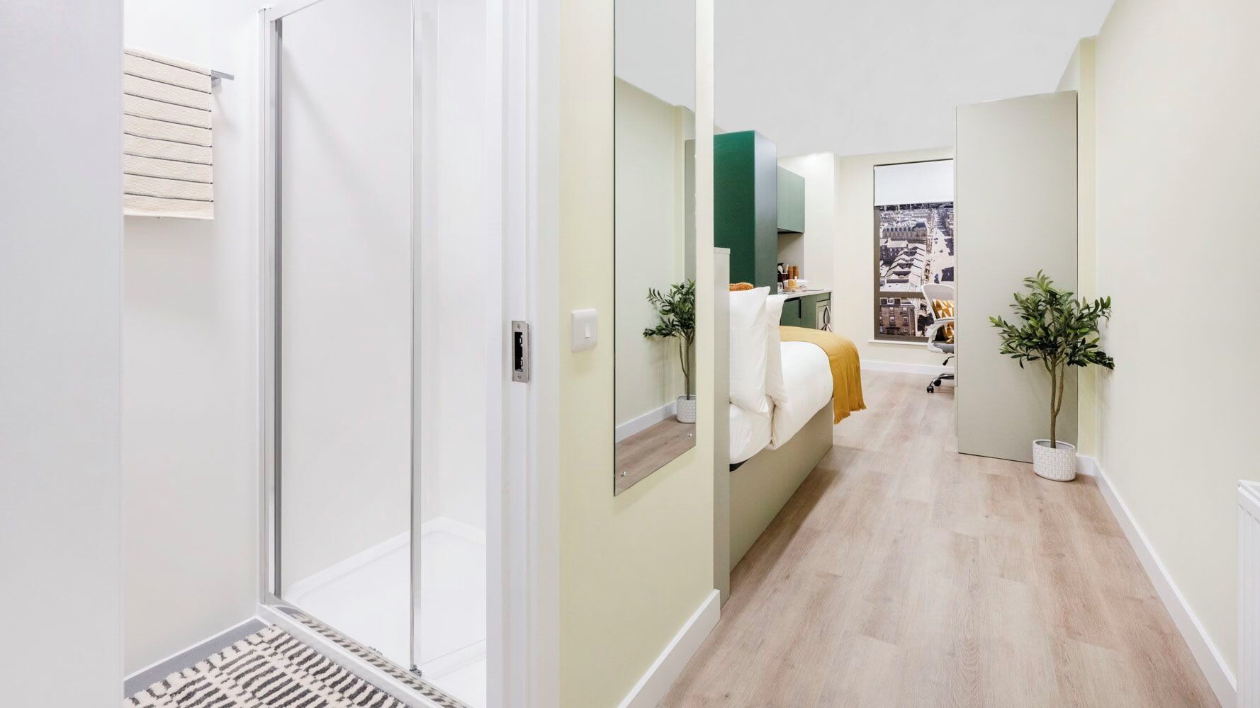 A hallway leading to a bedroom with a bed, a mirror, and a window.
